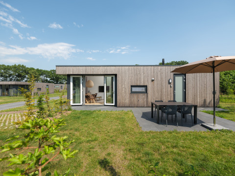 Moderne Holzhütte mit Terrasse, Esstisch und Sonnenschirm im Vakantiepark Hölte in den Niederlanden.