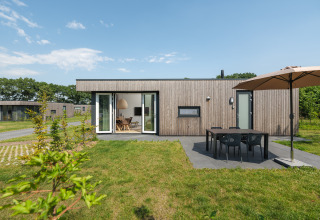 Moderne Holzhütte mit Terrasse, Esstisch und Sonnenschirm im Vakantiepark Hölte in den Niederlanden.