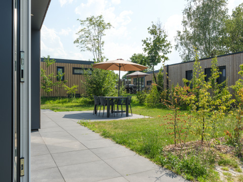 Udendørs terrasse ved Oak Lodge på Vakantiepark Hölte, Nederlandene, med borde, stole og parasol.