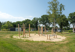 Playground with wooden structures on sand, surrounded by grass, near Oak lodge at Vakantiepark Hölte.