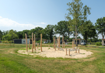 Speelplaats met houten toestellen op zand bij Oak lodge in Vakantiepark Hölte, omgeven door groen.