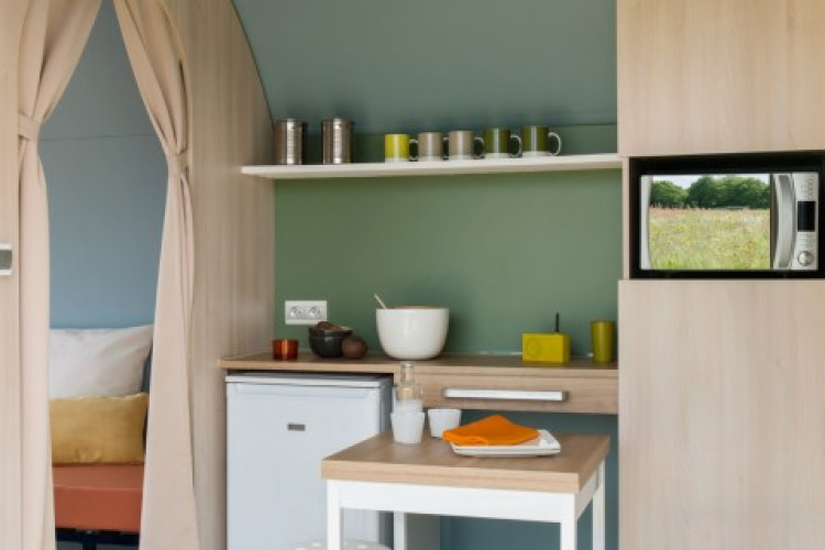 Interior de la tienda safari Coco Sweet en Camping Seasonova Haliotis, Francia, con área de cocina pequeña.