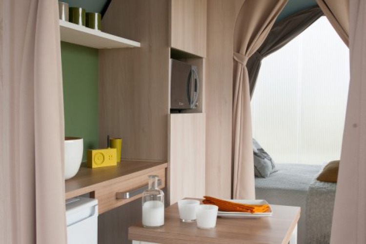 Vista interior de una tienda safari Coco Sweet en Camping Seasonova Haliotis, Francia, con cocina y cama visible.