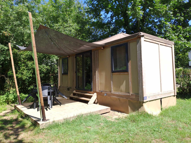 Photo of the Corfou cabin with covered deck, outdoor chairs and table amidst green, wooded surroundings.