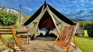 Tenda tipi Nomad Bivouac con pedana in legno, sedie e tavolo in un giardino verde sotto cielo nuvoloso.