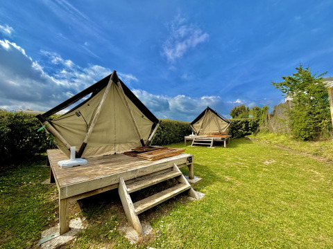 Twee glamping-tenten op houten platforms in een groene tuin onder een blauwe lucht met enkele wolken.