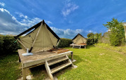 Twee glamping-tenten op houten platforms in een groene tuin onder een blauwe lucht met enkele wolken.