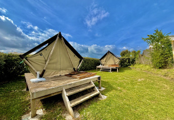 Twee glamping-tenten op houten platforms in een groene tuin onder een blauwe lucht met enkele wolken.