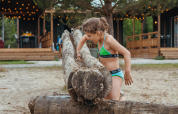 Fille en bikini vert grimpant sur des troncs à Tiny Wander Lodge au Holiday Park Sallandshoeve, Pays-Bas.
