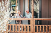 Couple senior assis et discutant sur la terrasse en bois du Tiny Wander Lodge lors d'une journée ensoleillée.