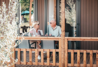 Couple senior assis et discutant sur la terrasse en bois du Tiny Wander Lodge lors d'une journée ensoleillée.