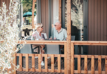 Couple senior assis et discutant sur la terrasse en bois du Tiny Wander Lodge lors d'une journée ensoleillée.