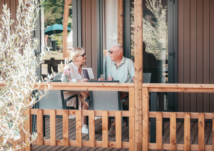 Ouder stel praat samen op de houten veranda van Tiny Wander Lodge tijdens een zonnige dag.