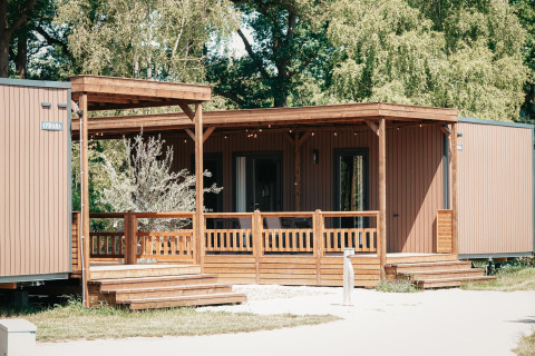 Vista exterior de Tiny Wander Lodge, una cabaña de madera moderna con porche, rodeada de árboles verdes.