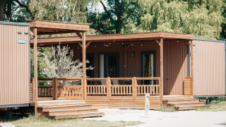 Vue extérieure du Tiny Wander Lodge, une cabane en bois moderne avec véranda, entourée d'arbres verts.