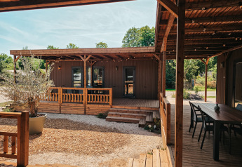 Vue extérieure de la Tiny Wander Lodge avec terrasse en bois, coin salon et verdure environnante.