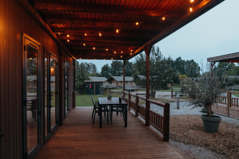 Terraza de madera con luces y mesa en Tiny Wander Lodge, Holiday Park Sallandshoeve, Países Bajos.