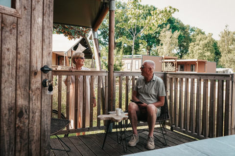 Ældre par nyder morgenkaffen på terrassen ved en luksus safaritelts hytte i Holiday Park Sallandshoeve.