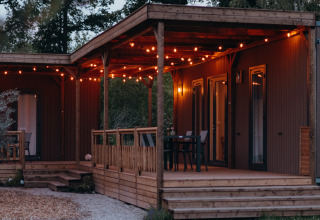 Vue du soir du Tiny Wander Lodge au Holiday Park Sallandshoeve, guirlandes lumineuses sur la terrasse en bois.