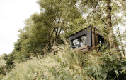 La Nokken NKN-18 Cabin, une tiny house moderne, nichée sur une colline entourée d’arbres et de verdure.