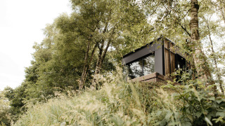 De Nokken NKN-18 Cabin, een moderne tiny house, genesteld op een helling tussen bomen en weelderig groen.