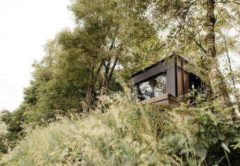 Nokken NKN-18 Cabin, en moderne tiny house, gemt blandt træerne på en skråning og omgivet af frodig natur.
