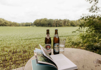 Dos cervezas, un vaso de agua y un libro abierto sobre una mesa con vistas a Nokken NKN-18 Cabin, Wilsumer Berge.