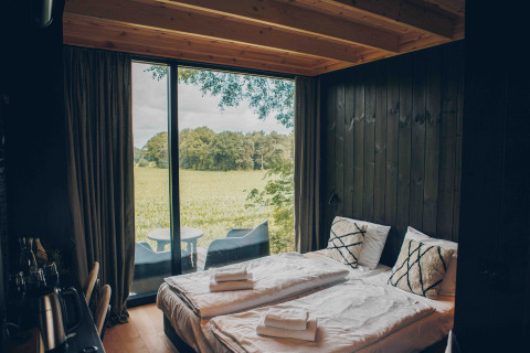 Minimalistisk soveværelse i Nokken NKN-18 Cabin ved Wilsumer Berge, Tyskland, med udsigt til mark.