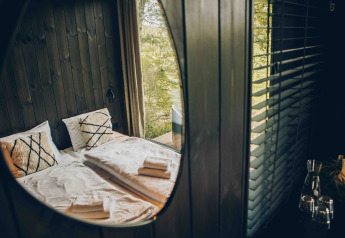 Refleksion af hyggelig soveplads i Nokken NKN-18 Cabin ved Wilsumer Berge, Tyskland, gennem et vindue.
