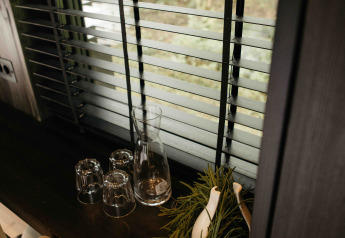 Intérieur du Nokken NKN-18 Cabin à Wilsumer Berge, Allemagne, avec carafe, verres et herbes près de la fenêtre.