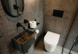 Salle de bain moderne dans la cabine Nokken NKN-18 à Wilsumer Berge, Allemagne, avec lavabo sombre et WC blanc.