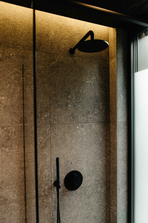 Modern shower with black fixtures and gray tiles in the Nokken NKN-18 Cabin at Wilsumer Berge, Germany.