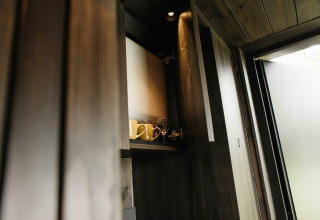 Åben køkkenskab i Nokken NKN-18 Cabin ved Wilsumer Berge, Tyskland, med krus og vinglas.