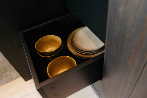Gold-colored bowls and white plates neatly stored in a black drawer at Nokken NKN-18 Cabin, Germany.