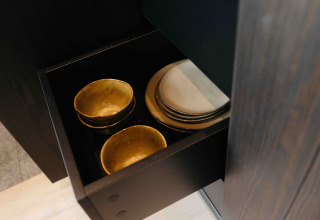 Ciotole dorate e piatti bianchi ordinatamente disposti in un cassetto nero al Nokken NKN-18 Cabin in Germania.