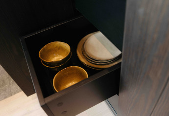 Goldfarbene Schalen und weiße Teller in einer schwarzen Schublade in der Nokken NKN-18 Cabin, Deutschland.