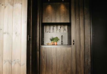 Kleine moderne Küchenzeile mit Holzverkleidung, Kräutertöpfen und Spüle in einer Nokken NKN-18 Cabin bei Wilsumer Berge, Deutschland.