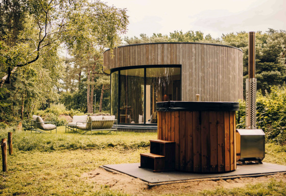 Modernes rundes LumiPod Tiny House mit großen Fenstern, Holzfassade und Whirlpool im Grünen.