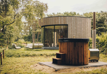 Casa tiny house LumiPod circolare con ampie vetrate, rivestimento in legno e vasca idromassaggio esterna.