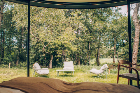 Blick aus einem Tiny House mit großen Fenstern auf Gartenmöbel und Wald am Wilsumer Berge in Deutschland.