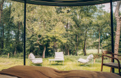 Vue depuis l'intérieur d'une tiny house sur des fauteuils extérieurs, une table et la forêt à Wilsumer Berge, Allemagne.