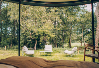 Blick aus einem Tiny House mit großen Fenstern auf Gartenmöbel und Wald am Wilsumer Berge in Deutschland.