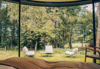 Vue depuis l'intérieur d'une tiny house sur des fauteuils extérieurs, une table et la forêt à Wilsumer Berge, Allemagne.