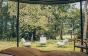 Zicht vanuit een tiny house met grote ramen op stoelen, tafel en bos bij Wilsumer Berge in Duitsland.