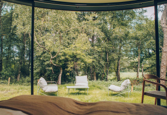 Vista dall’interno di una tiny house verso sedie, tavolo e bosco presso Wilsumer Berge in Germania.