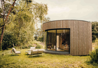 Tiny house ronde en bois à grande baie vitrée, mobilier de jardin sur pelouse, à Wilsumer Berge, Allemagne.