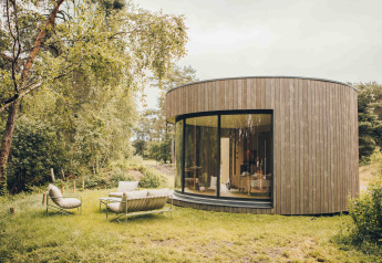 Tiny house rotonda in legno con grandi finestre curve e sedute esterne a Wilsumer Berge, Germania.