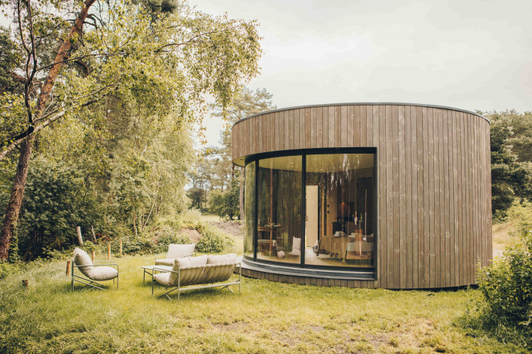 Rond, houten tiny house met grote glazen pui en buitenzitjes in het groen bij Wilsumer Berge, Duitsland.
