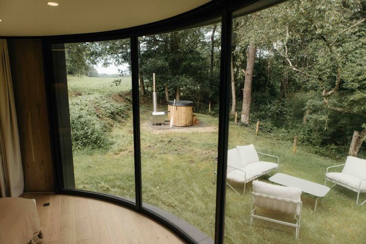 Blick aus LumiPod mit Hot Tub bei Wilsumer Berge, Deutschland, mit großen Fenstern und Lounge im Grünen.