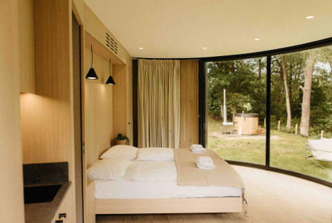 Modern slaapkamerinterieur in LumiPod tiny house bij Wilsumer Berge, Duitsland, met panoramavenster en hot tub.